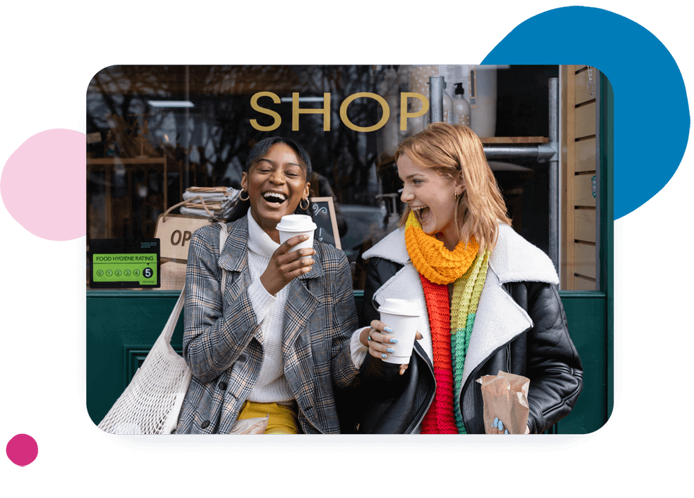 Two people laughing and holding cups outside a coffee shop